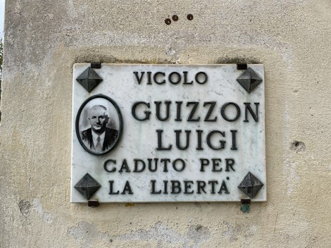 Lapide commemorativa in marmo dedicata a Luigi Guizzon, situata in un vicolo, con un ritratto ed epigrafe.