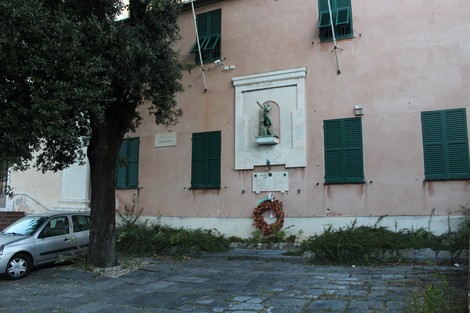 Lapidi commemorative ai caduti in un contesto urbano, con un monumento e un albero nelle vicinanze.