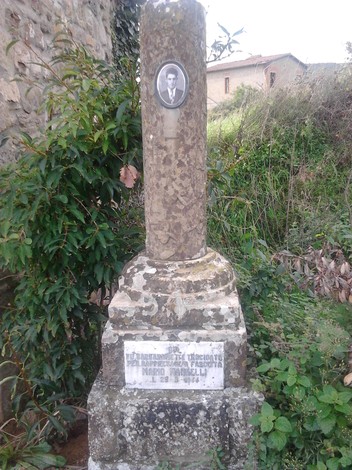 Cippo commemorativo in memoria di Mannelli, con fotografia e iscrizioni, immerso nella natura circostante.
