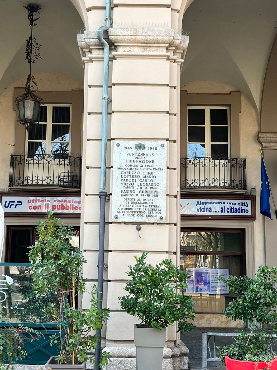 Lapide commemorativa che celebra il ventennale della Liberazione, situata su un pilastro di un edificio storico.