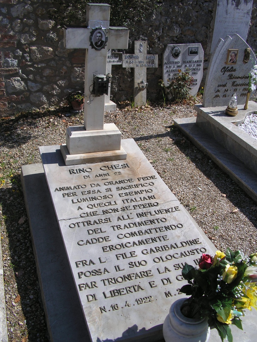 Sepolcro di Rino Chiesi, con croce, decorazioni floreali e iscrizioni commemorative in un cimitero.