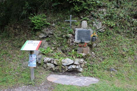 Lapide commemorativa in onore dei caduti per la libertà, con fiori e croce, immersa nella natura.