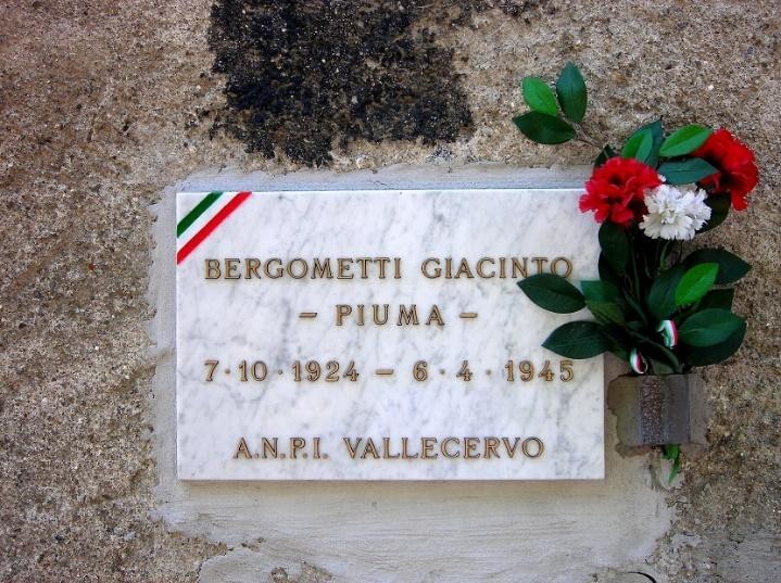 Lapide commemorativa dedicata a Giacinto Bergometti, con fiori in omaggio e simboli nazionali.