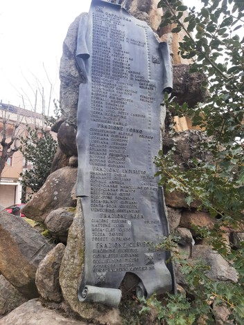 Monumento ai caduti con una stele commemorativa e dettagli di iscrizioni su un supporto roccioso.