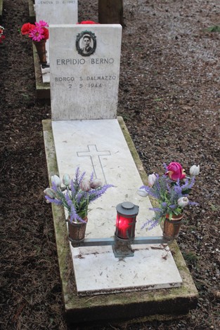 Tomba con lapide in marmo, decorata con fiori e una lanterna, in memoria di un caduto per la libertà.