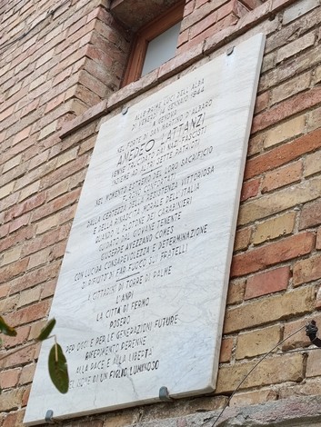 Lapide in onore di Lattanzi, recante un testo commemorativo su una facciata in mattoni.
