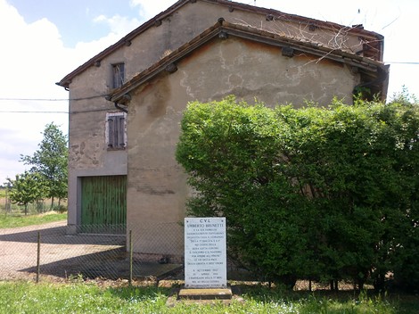 Monumento alla famiglia Brunetti, situato in un'area rurale, con un edificio storico sullo sfondo.