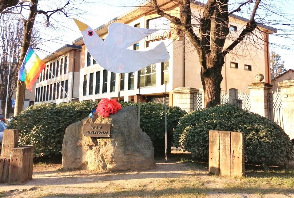 Monumento alla Resistenza con simbolo di pace e bandiera arcobaleno, in un contesto urbano.