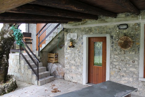 Lapide commemorativa su un muro di pietra, con scalini e ingresso in legno. Ambiente rustico e naturale.