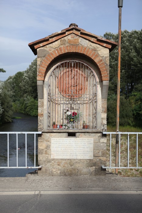 Lapide del ponte di Annibale, monumento storico con decorazioni e fiori, situato lungo un corso d'acqua.