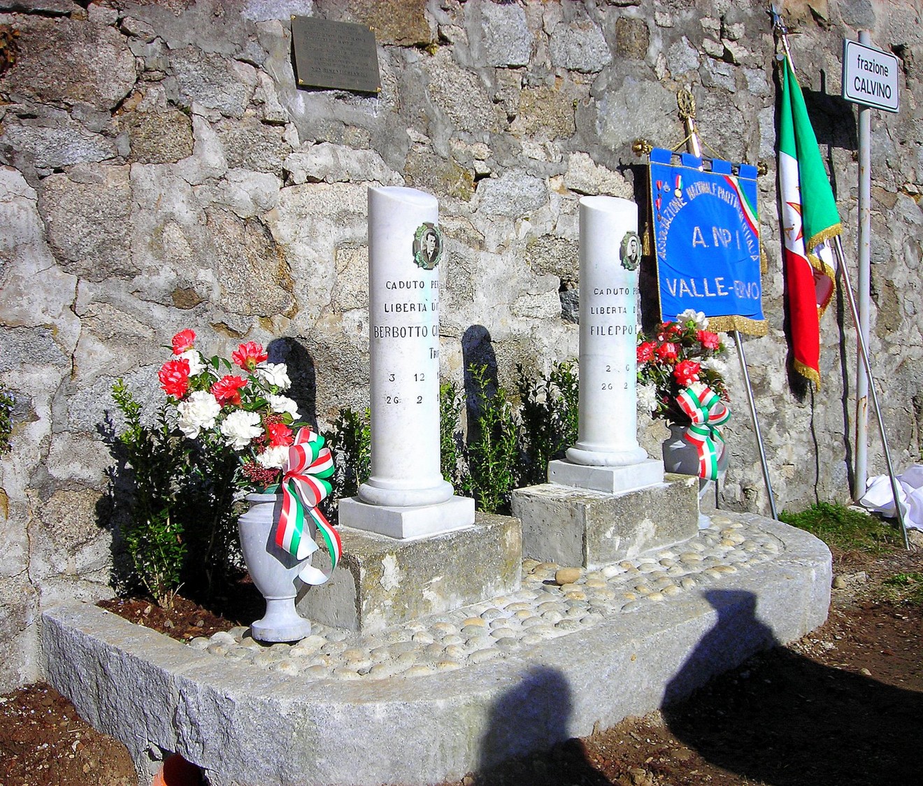 Cippi commemorativi di Berbotto e Fileppo, con decorazioni floreali e bandiera italiana sullo sfondo.