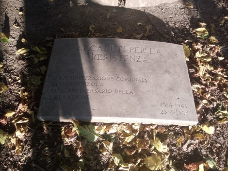 Lapide commemorativa dedicata ai caduti per la Resistenza, immersa nel verde e circondata da foglie.