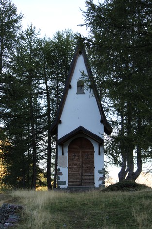 Cappelletta ai Partigiani immersa tra alberi, con ingresso in legno e tetto a spiovente, simbolo di memoria storica.