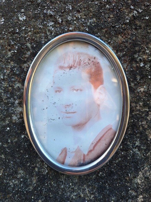 Medaglione ovale con ritratto fotografico di un giovane, inserito in una cornice metallica su roccia.