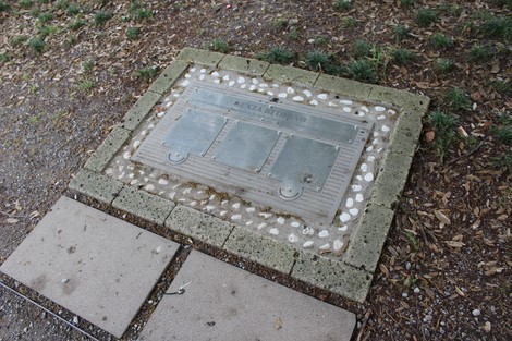 Monumento ai deportati caduti, una placca commemorativa incastonata nel pavimento, circondata da ghiaia e mattonelle.