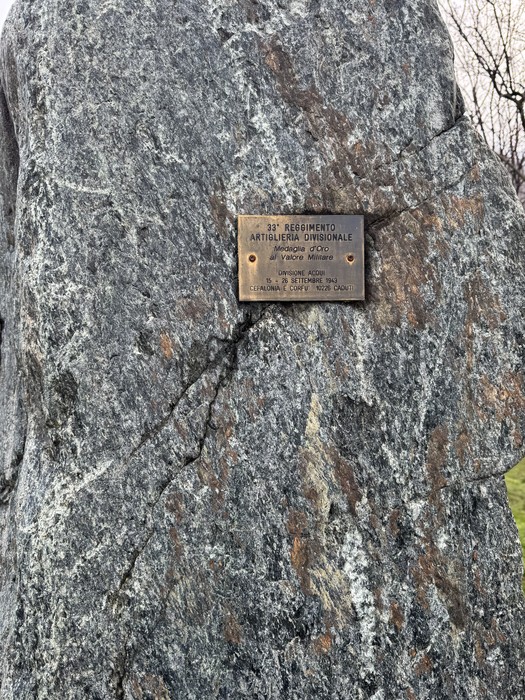 Targa in metallo con iscrizione, fissata su un masso di roccia grezza all'aperto.