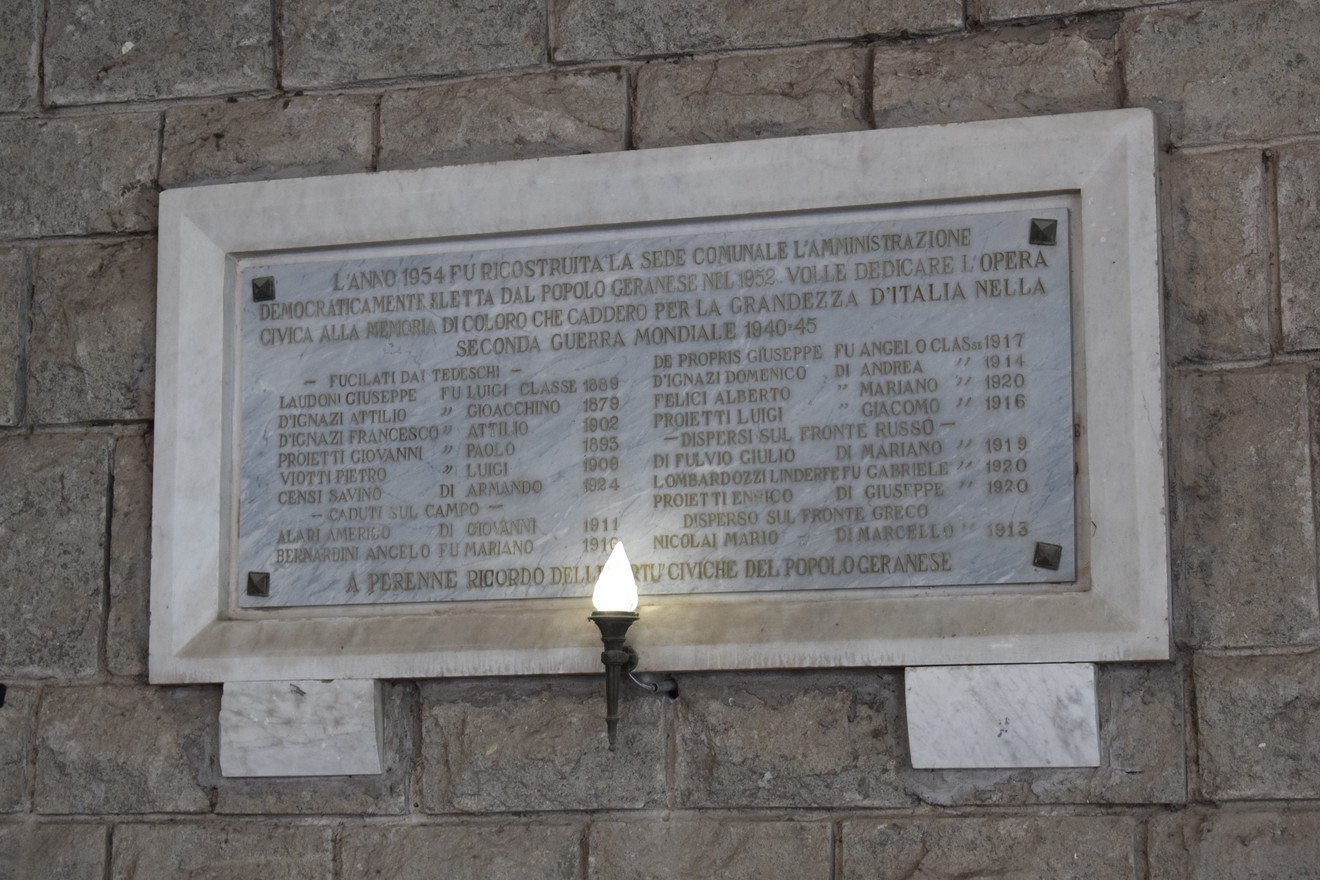 Lapide commemorativa con targa dedicata ai caduti in guerra, incastonata in una parete di pietra.