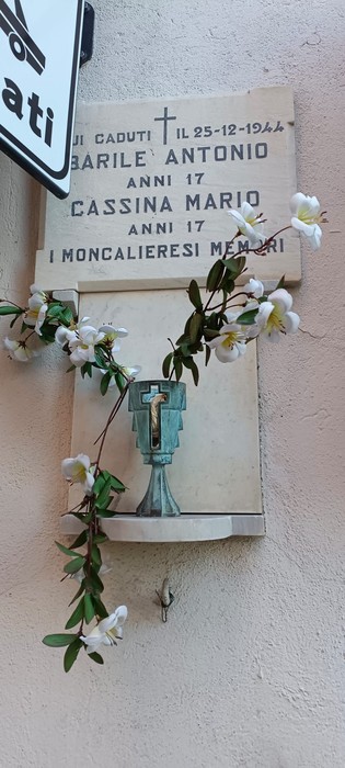 Lapide commemorativa con fiori, dedicata a Barile e Cassina, raffigurante una croce e nomi di caduti.