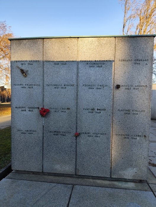 Monumento commemorativo con nomi incisi, dedicato ai caduti, decorato con fiori e simboli di rispetto.