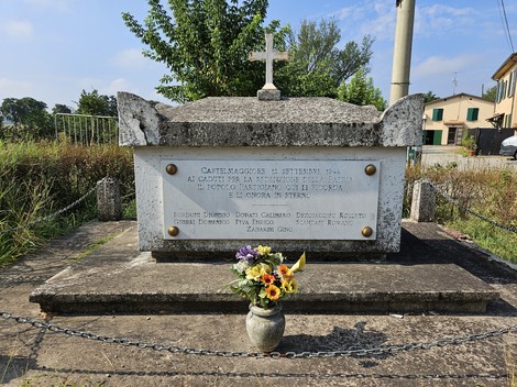 Monumento commemorativo ai Martiri della Biscia, con decorazioni floreali e croce in cima.