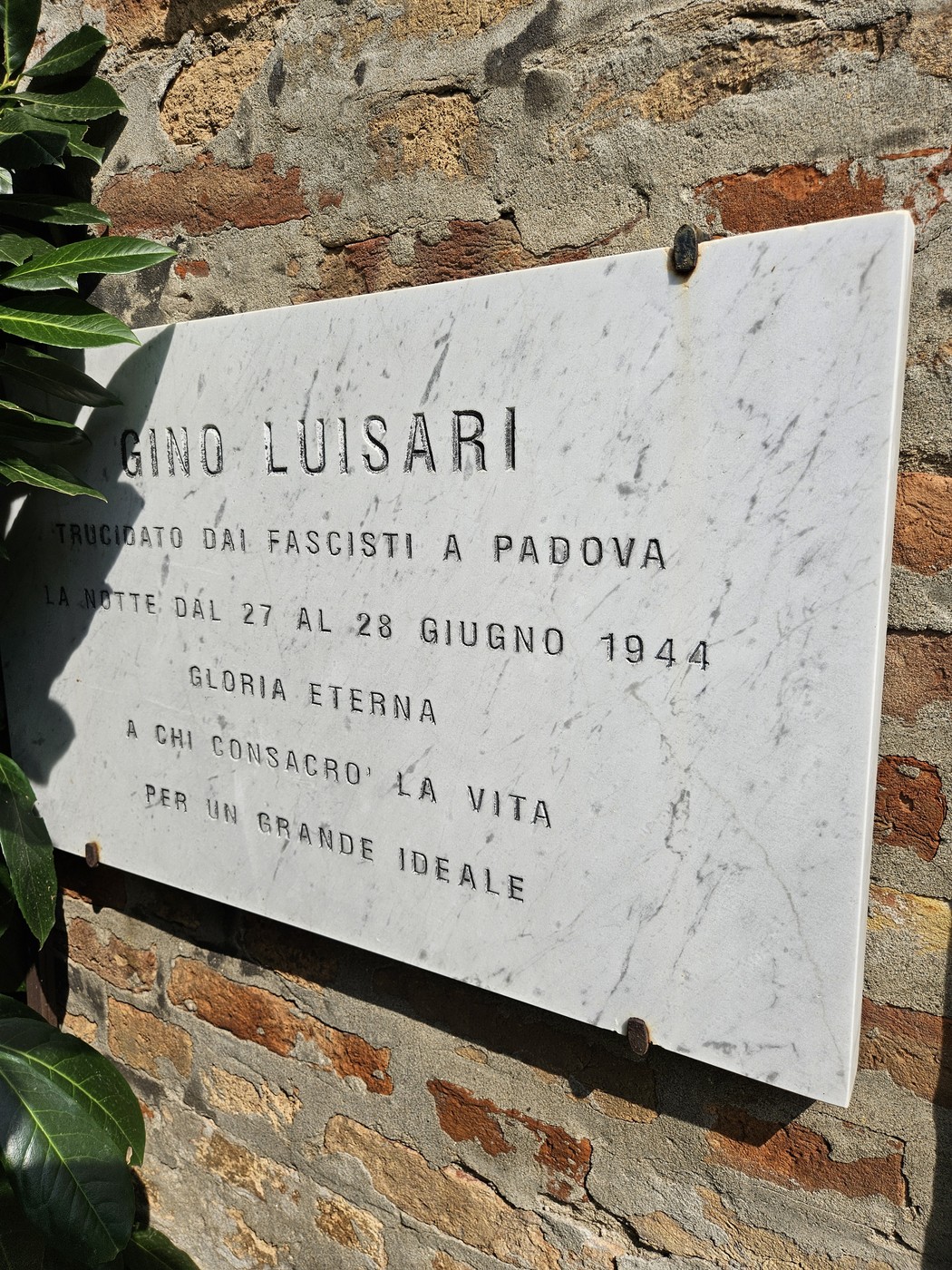 Lapide commemorativa dedicata a Gino Luisari, martire della Resistenza, affissa su muro di pietra.