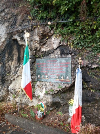 Lapide commemorativa della strage della Montagnetta di Fiumelatte con bandiere e fiori.