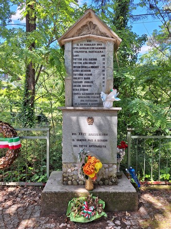 Monumento dedicato ai giovani partigiani, con iscrizioni commemorative e adornato da fiori e simboli tricolore.