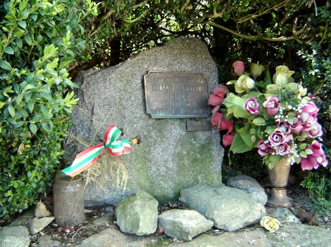 Cippo commemorativo dedicato ad Alberto, adornato con fiori e un nastro tricolore.