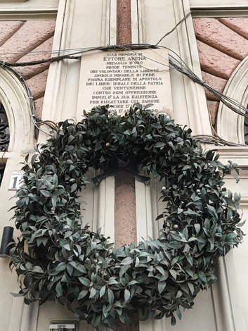 Lapide commemorativa con una corona di foglie verdi, situata su una parete in città.