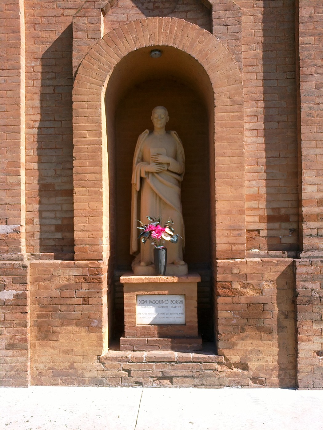 Statua di Borghi, situata in un'arcata di mattoni, con un vaso di fiori ai suoi piedi.