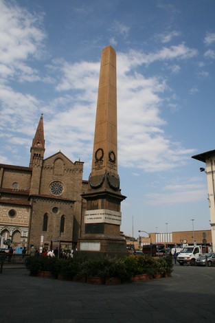 Obelisco ai caduti, monumento commemorativo in Piazza della Libertà a Firenze, circondato da piante e architettura storica.