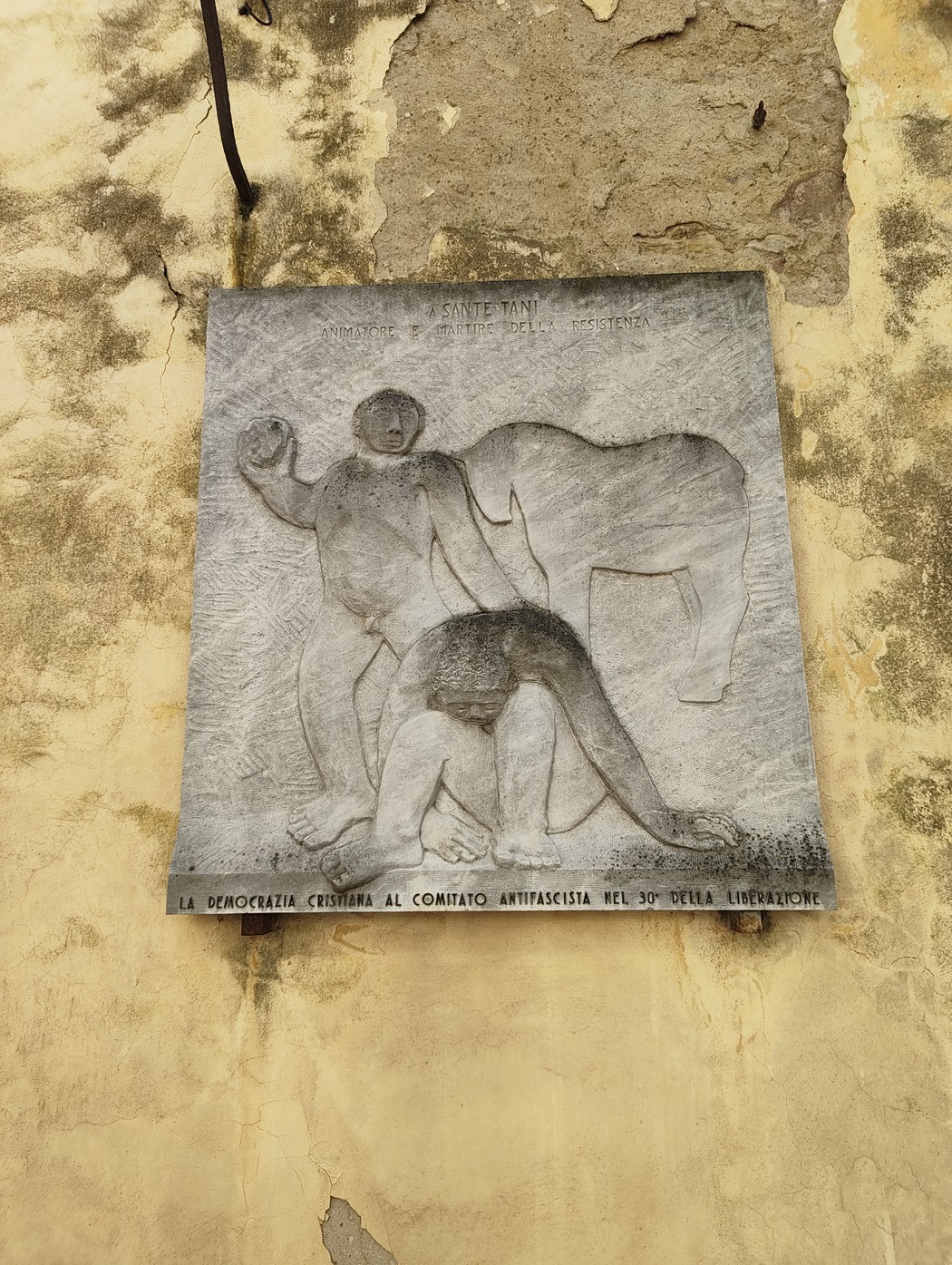 Bassorilievo artistico che rappresenta figure umane, con un forte contrasto su sfondo di parete ingrigita.