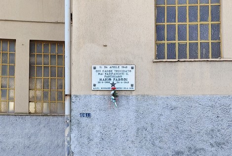 Lapide commemorativa dedicata a Mario Parodi, situata su un edificio, con decorazioni floreali.