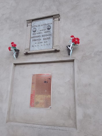Lapide commemorativa a Bertero e Ribotta, Città di Kioliana, con decorazioni floreali.