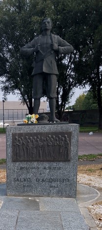 Monumento a D'Acquisto, con una statua che rappresenta un giovane in uniforme, circondato da decorazioni floreali.