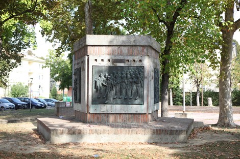 Monumento alla Resistenza, circondato da alberi, con pannelli commemorativi e un'area verde circostante.
