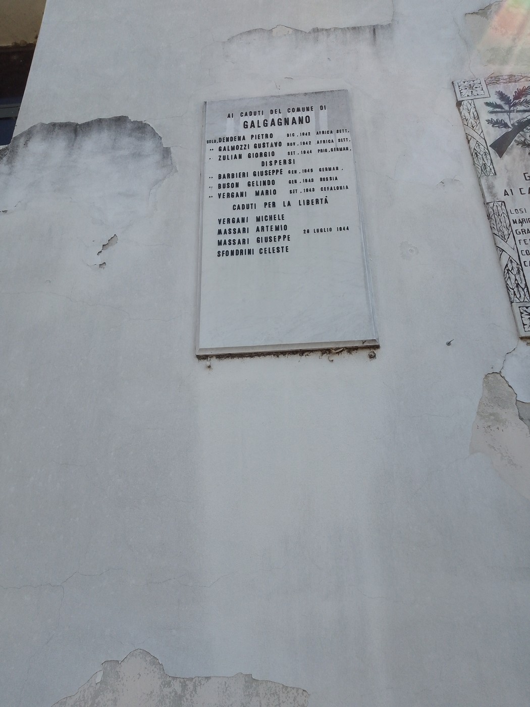 Lapide commemorativa su una parete, dedicata ai caduti in guerra, con nomi incisi e segni del tempo.