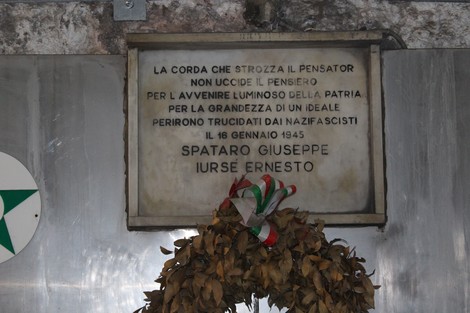 Lapide commemorativa dedicata a Spataro Giuseppe e Jursè Ernesto, con una corona di fiori e un messaggio di memoria storica.
