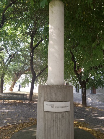 Monumento a Brambilla, colonna bianca circondata da alberi in un verde parco pubblico.