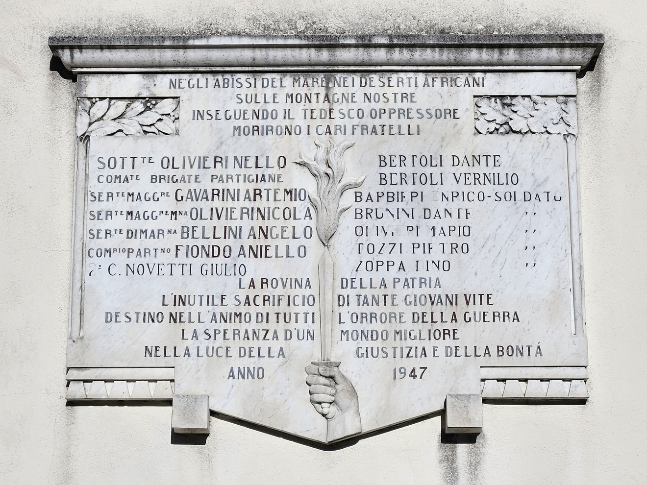 Lapide commemorativa ai caduti di Mocrone, con iscrizioni e decorazioni, situata in un contesto montano.