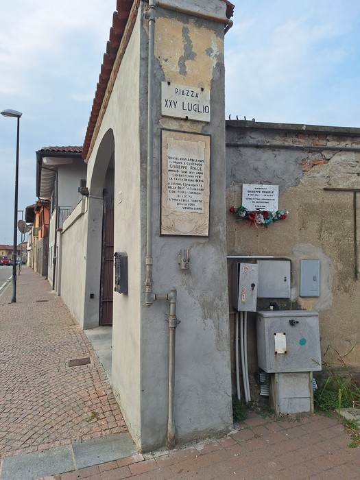 Lapide con iscrizione all'angolo di un edificio, sotto l'insegna di Piazza XXV Luglio.