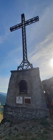 Croce monumentale su base in pietra, situata in uno scenario panoramico montano.
