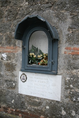 Lapide commemorativa a Chisci, partigiano di Belfego, con fiori celebrativi e dedica in memoria.