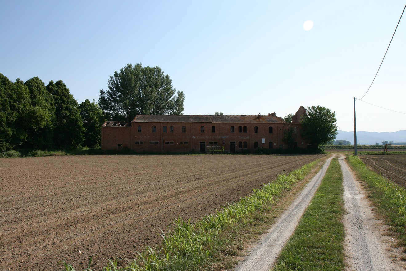 Lapide della Tabaccaia di Prato Grande, con vista su un edificio fatiscente e campi circostanti.