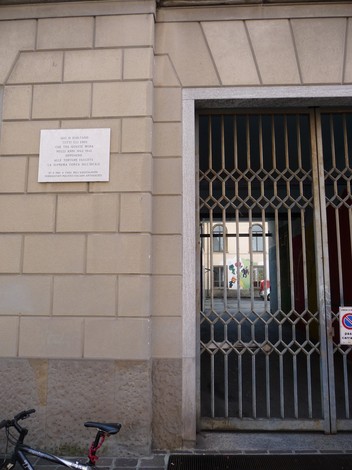 Lapide commemorativa alla memoria delle vittime di tortura in via Gallicciolli, con muro e porta chiusa sullo sfondo.