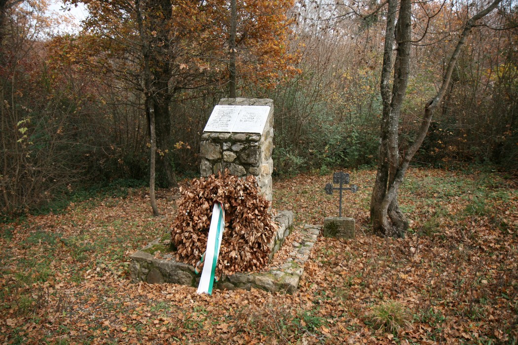 Cippo commemorativo dell'eccidio di Pratale, circondato da alberi e foglie secche nel contesto di un bosco.
