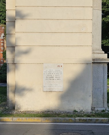 Lapide commemorativa dedicata a Riccardo Manzi, situata su un muro esterno, con dettagli architettonici circostanti.