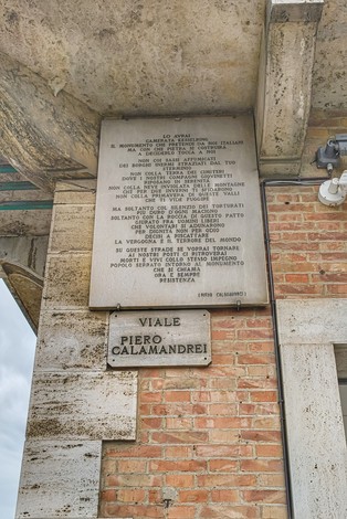 Lapide commemorativa in pietra, con iscrizioni storiche su tortura e ingiustizia, affissa su un muro in città.