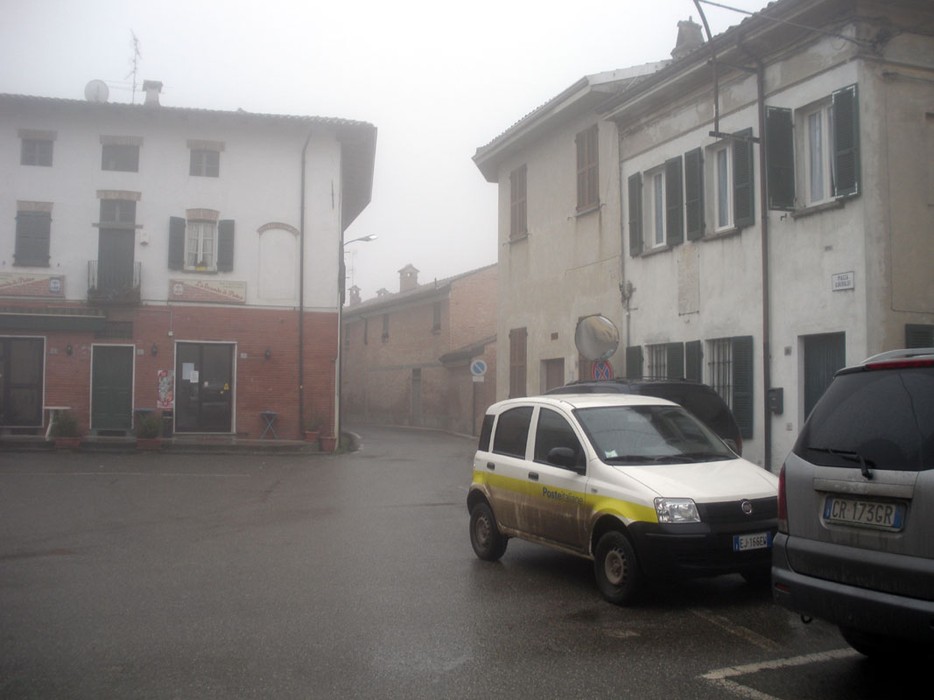 Lapide ai caduti di Pietra de' Giorgi in un'atmosfera nebbiosa. Ambiente urbano con edifici e auto.