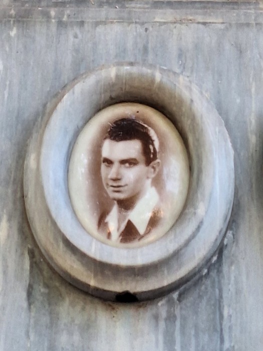Ritratto fotografico ovale di un giovane uomo, inserito in una cornice di marmo su parete.